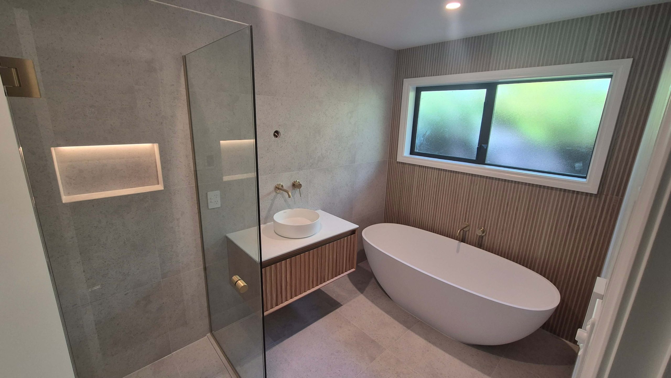 Modern bathroom design in Christchurch featuring brass tapware, stone-look tiles, and LED shower niche